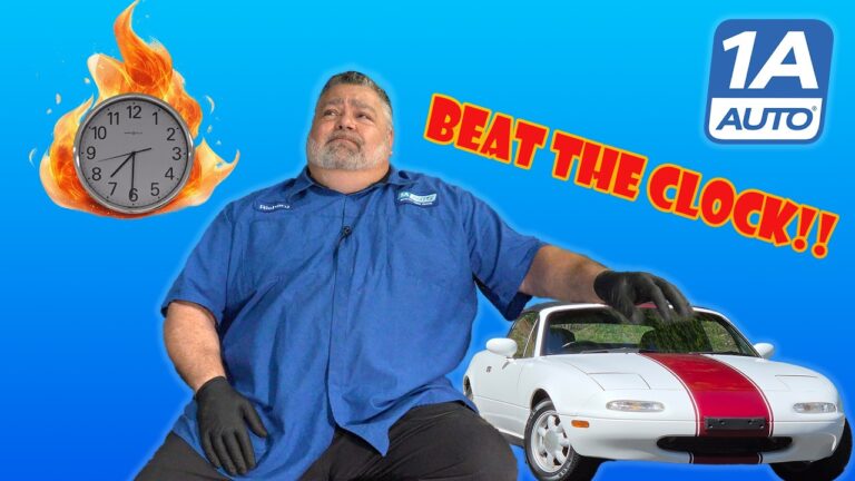 A mechanic working on the front brake assembly of a Mazda Miata in a garage.